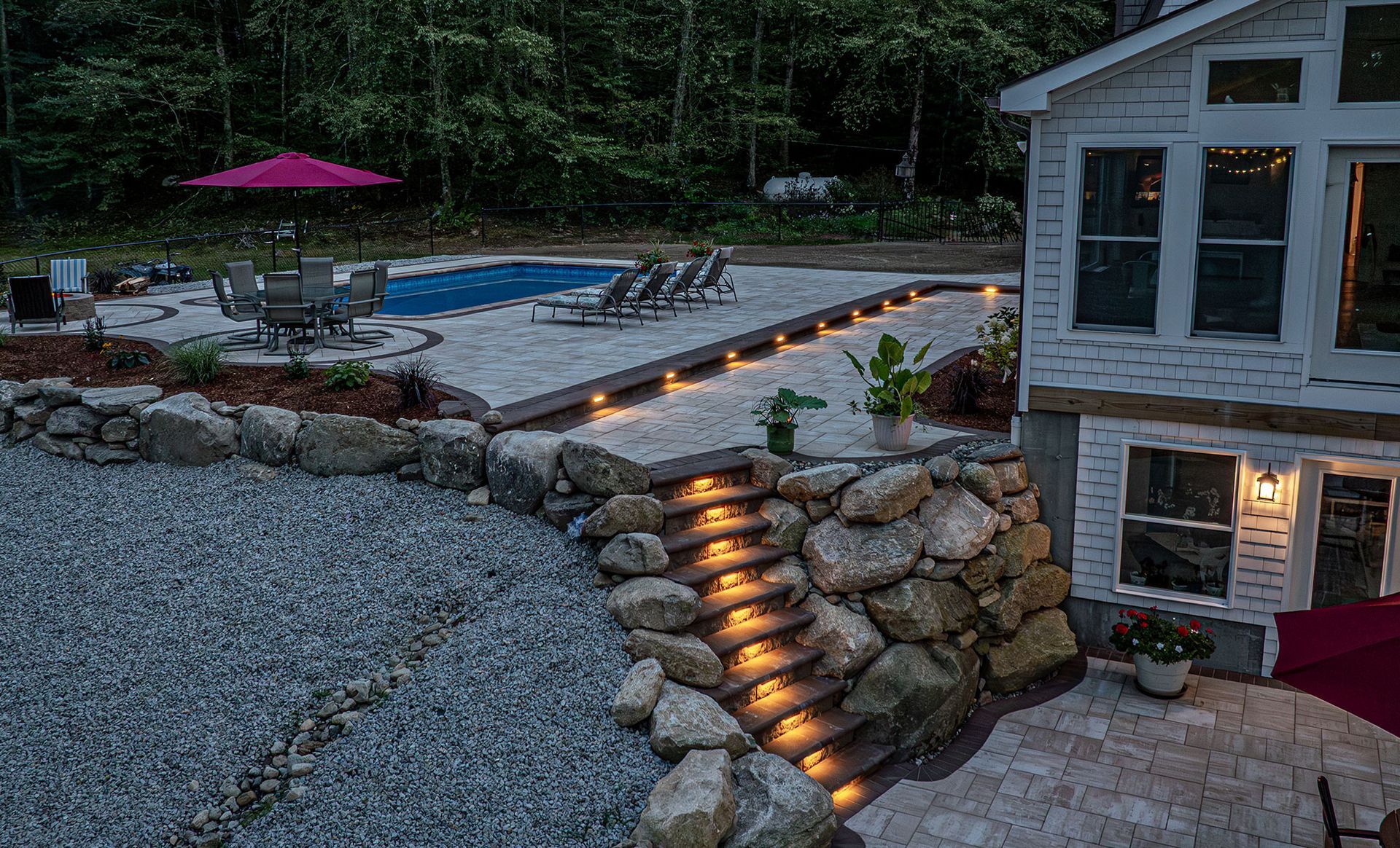 Nighttime backyard with a pool, patio, and stone steps illuminated by lights.