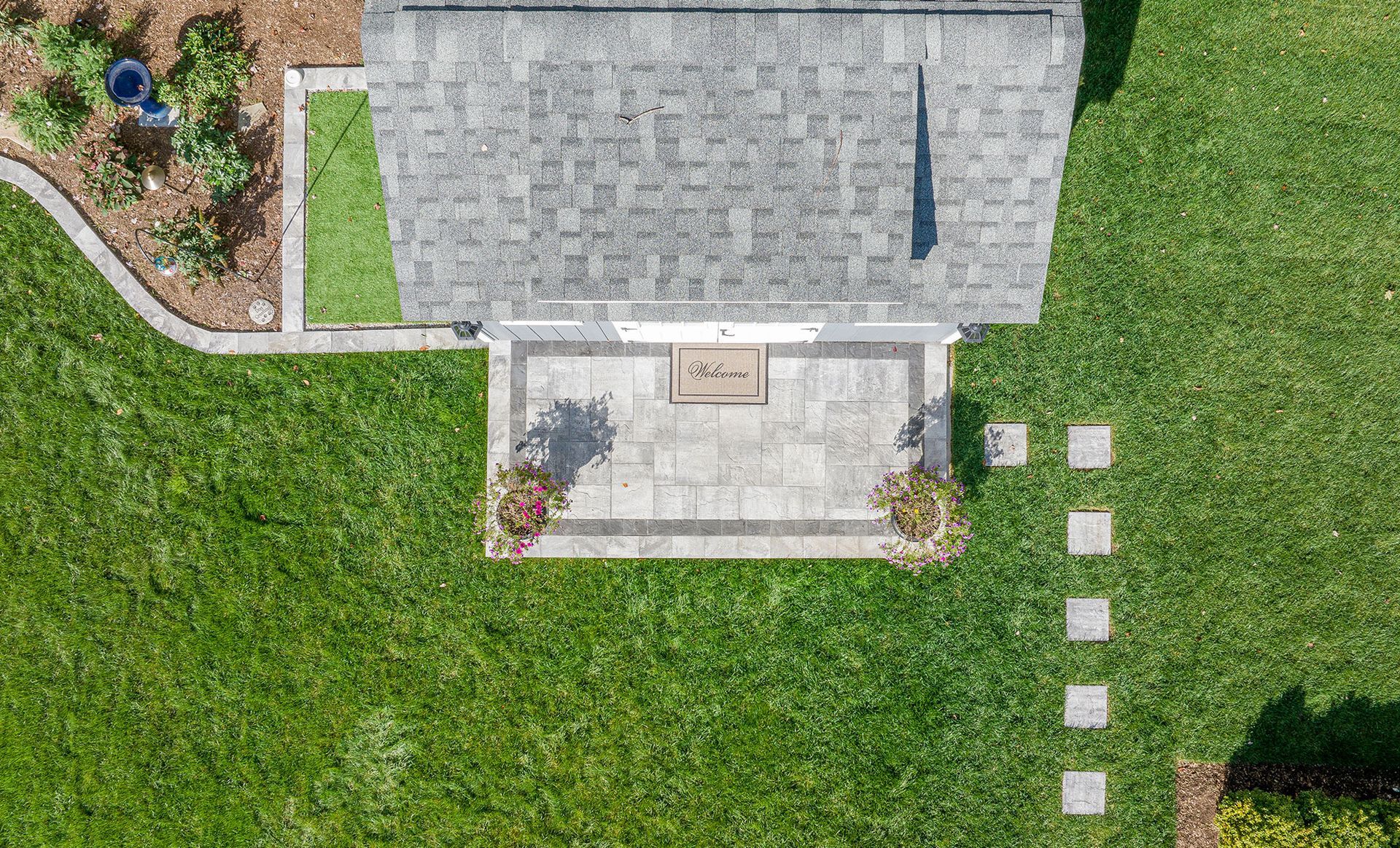 Overhead view of a house with a gray shingled roof, patio, and green lawn. Stepping stones lead to the patio.