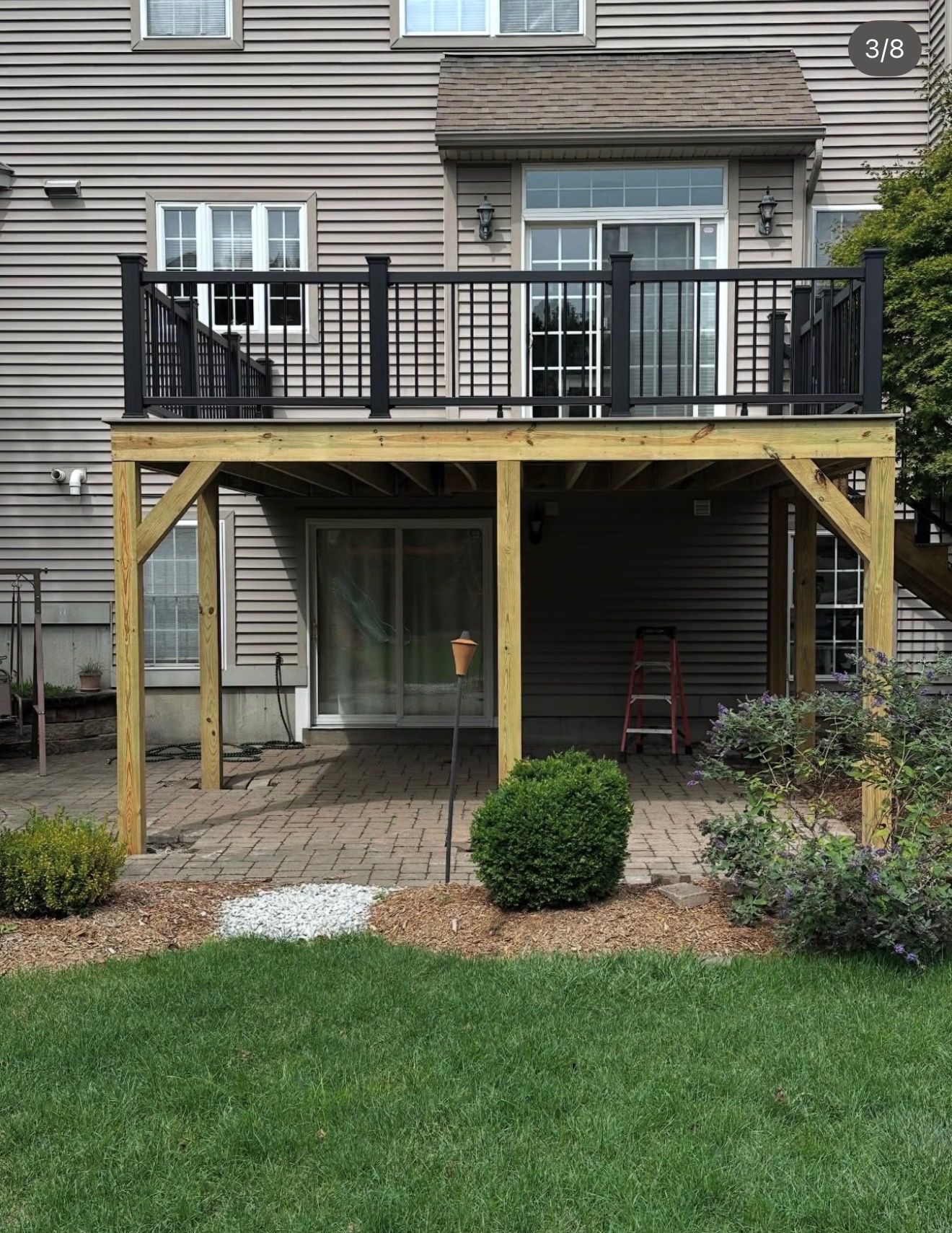 Backyard deck with black railing and yellow support posts under a gray house siding