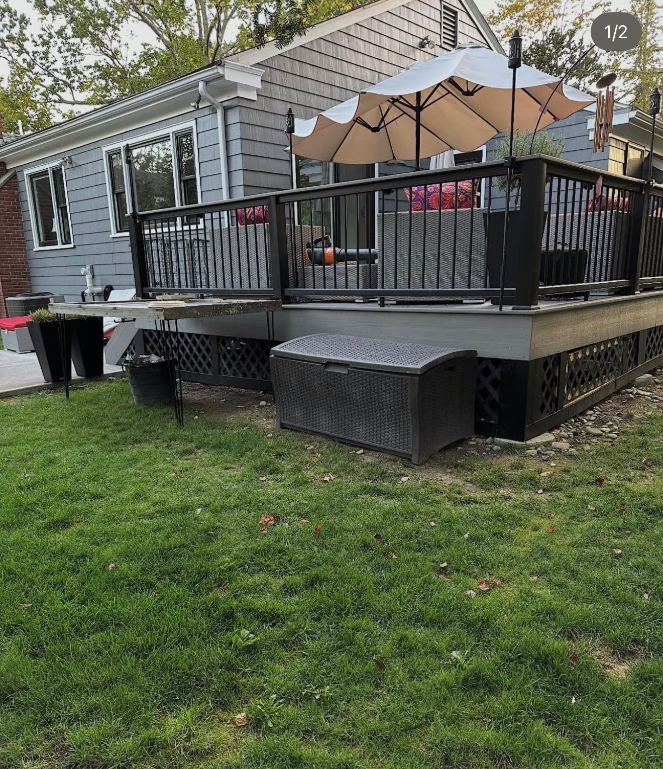 Raised backyard deck with black railing, tan umbrella, and outdoor furniture beside a grassy lawn