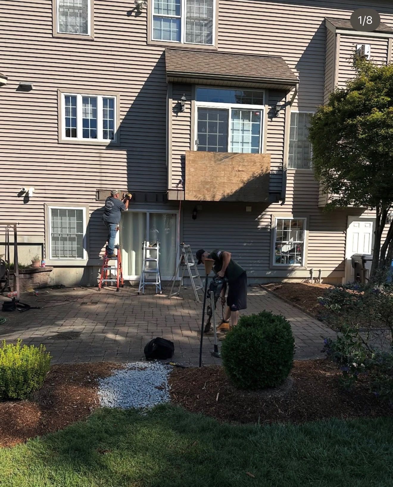 Workers tending a townhouse garden beneath a balcony under construction