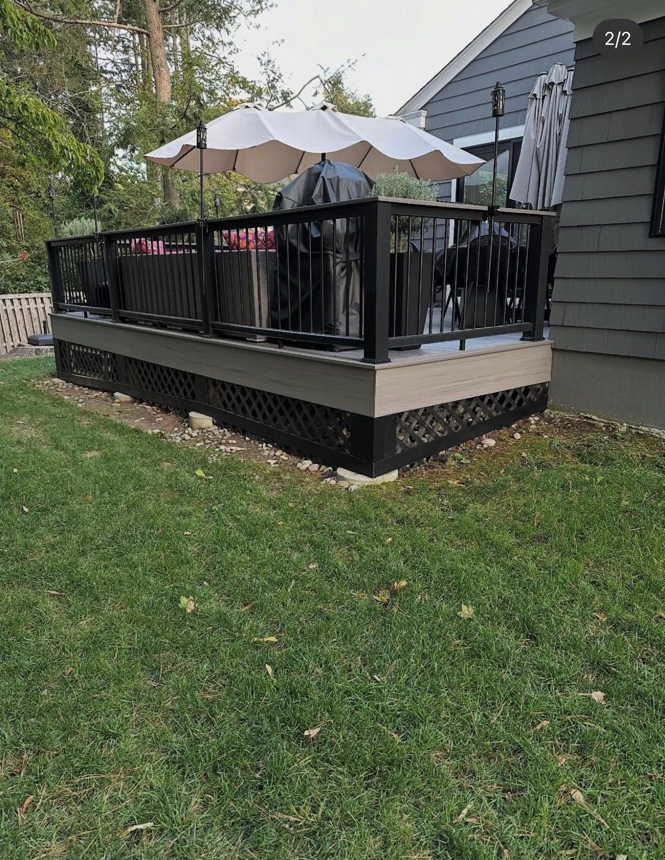 Outdoor deck with black railing, gray house siding, patio umbrella, and grill in a grassy yard