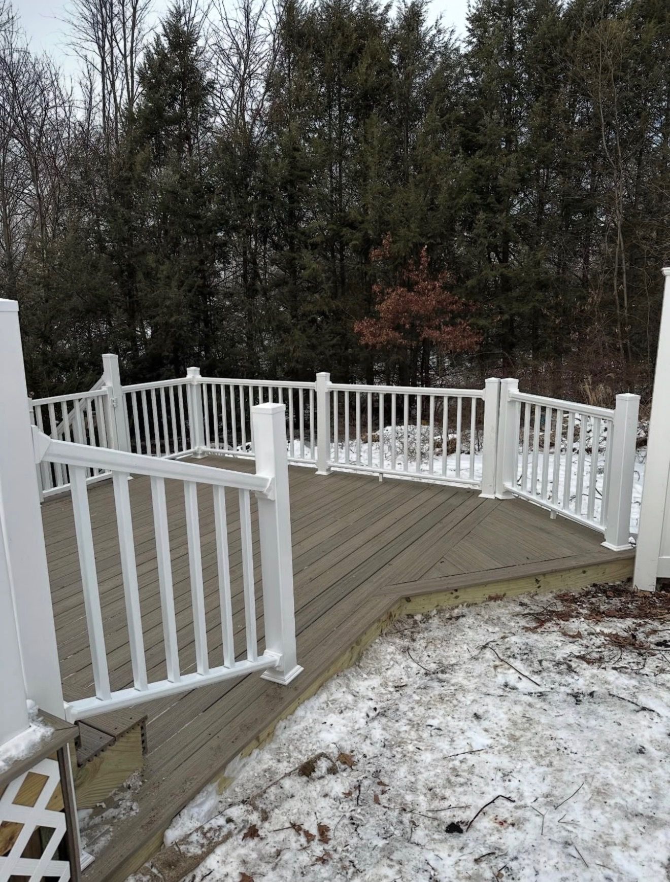 Wooden deck with white railings beside a snowy yard and trees