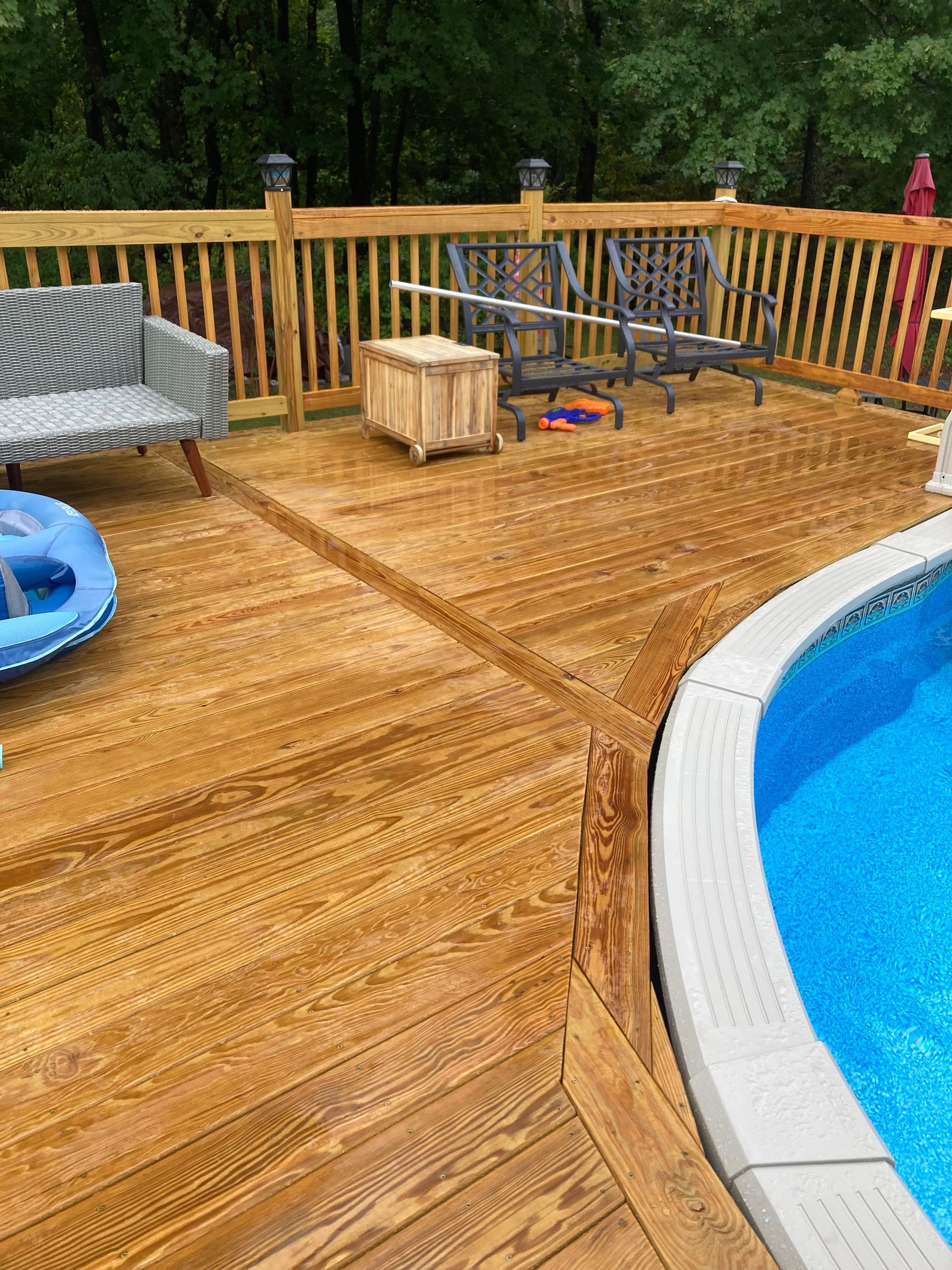 Wooden deck beside a blue pool, with outdoor chairs, a small table, and a crate near the railing