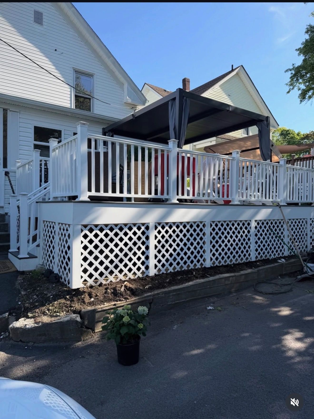 White house deck with white railings, black canopy, and lattice skirting beside a driveway