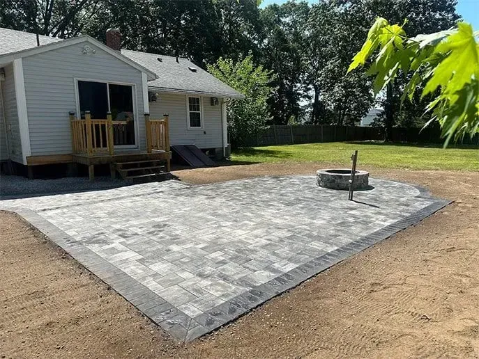 Backyard patio with gray pavers and a fire pit, near a house with a wooden deck.
