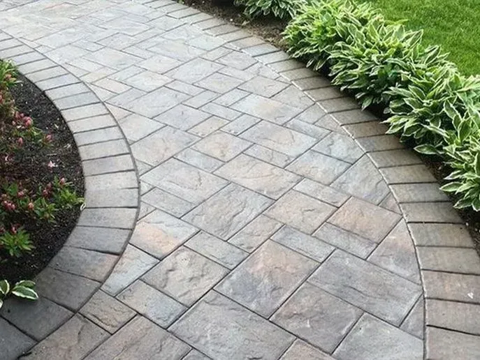 Brick pathway curving through a garden, bordered by plants and grass.