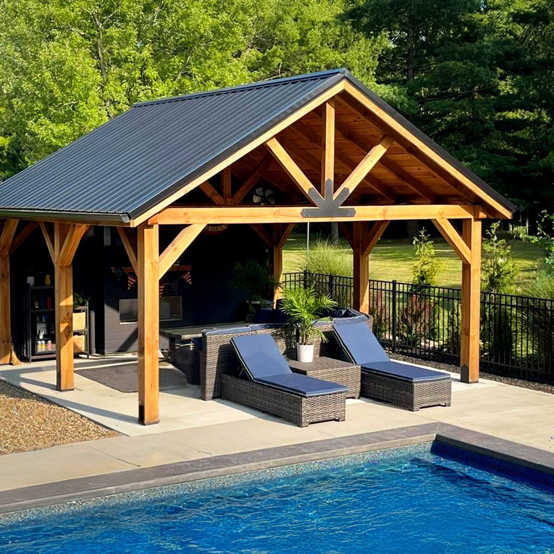 Outdoor wooden gazebo with blue roof, beside pool, with lounge chairs and seating.