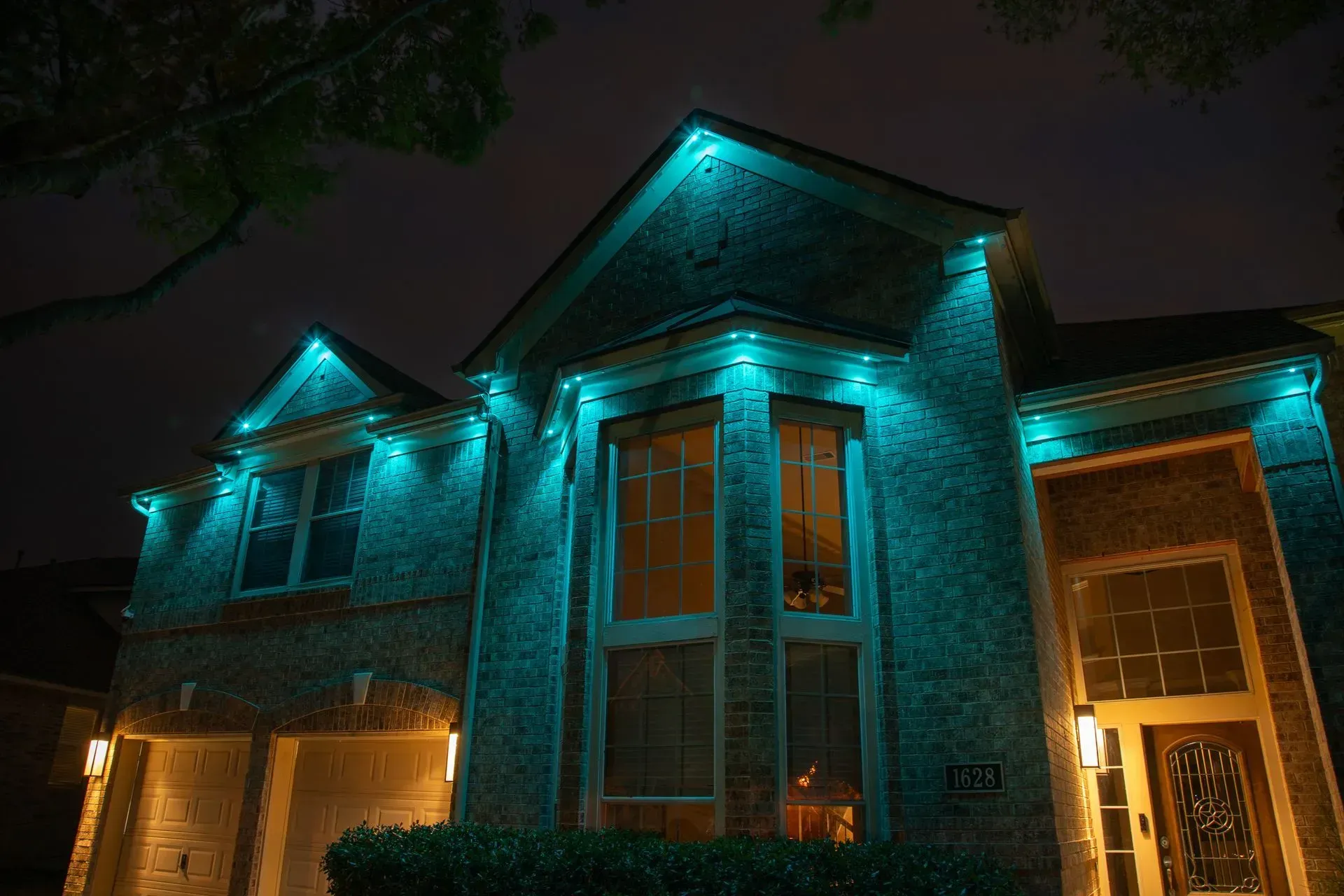 Two-story brick house illuminated with blue lights outlining roof and windows against a dark night sky.