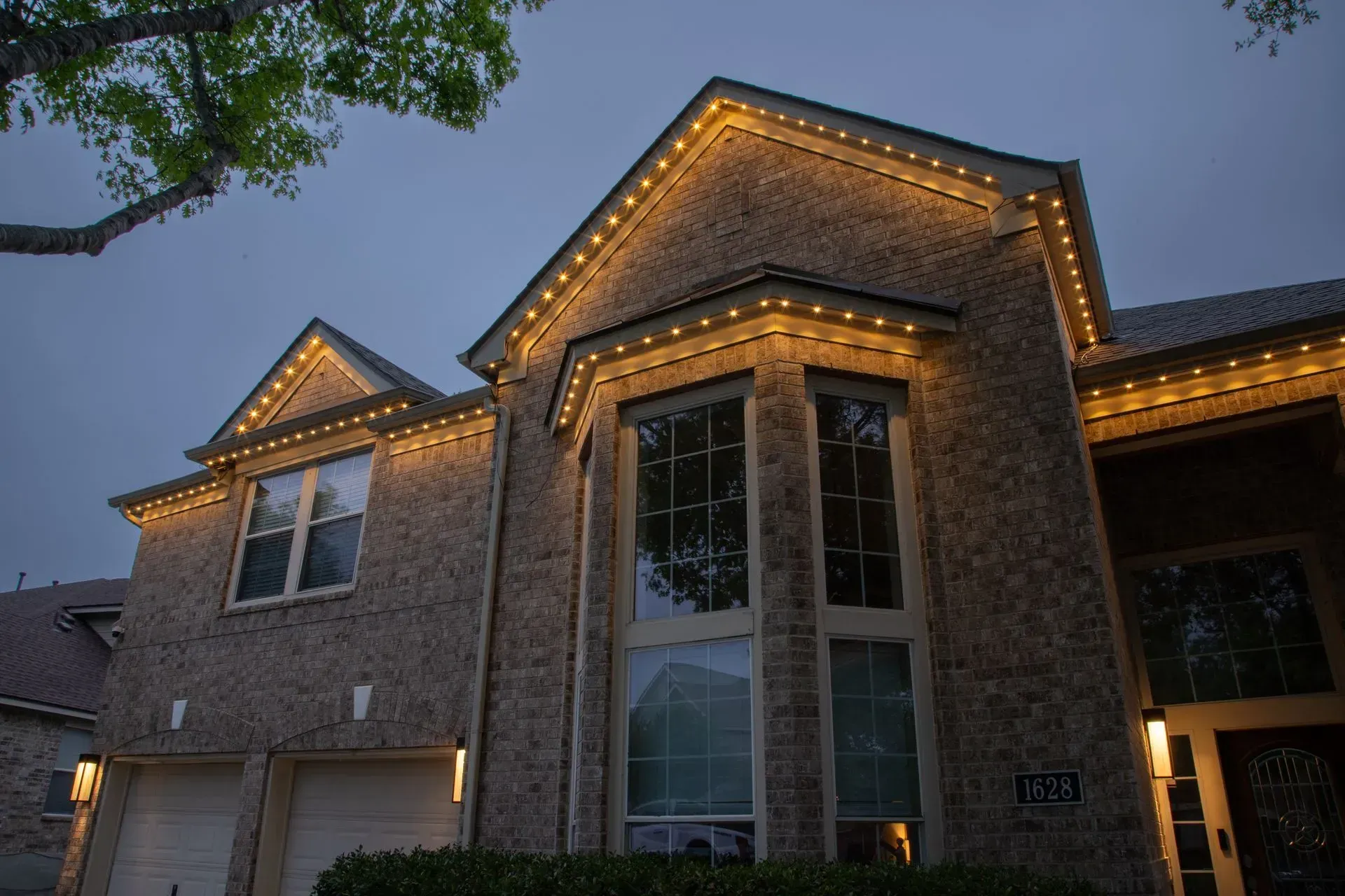 House with brick exterior, illuminated by warm white lights along the roofline.