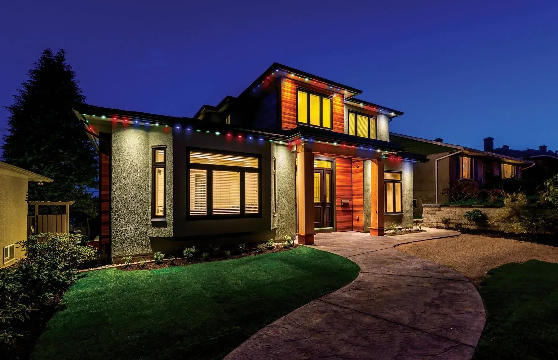 House exterior at night with Christmas lights, lighted windows, and a curved driveway.