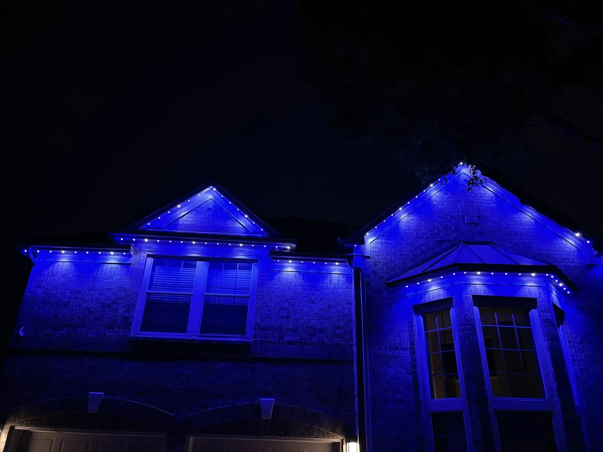 House with blue Christmas lights along the roof and windows against a dark night sky.