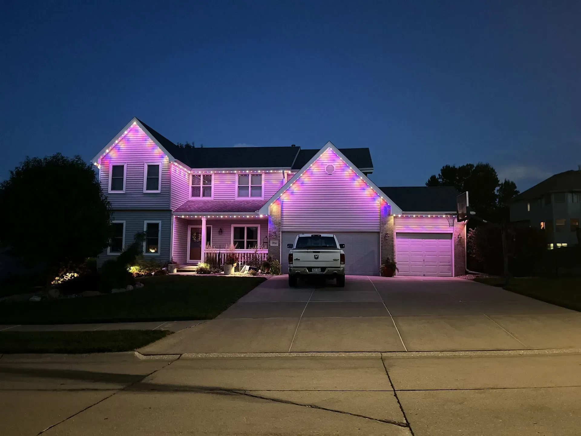 House with purple lights, white truck parked in the driveway, evening sky.