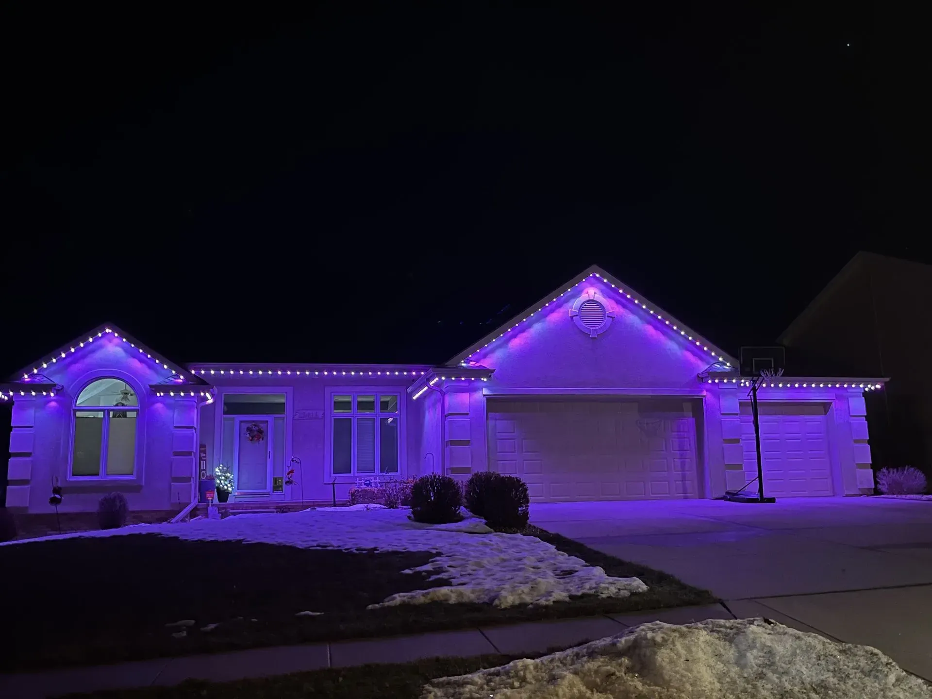House at night illuminated with purple lights, snow on the lawn.