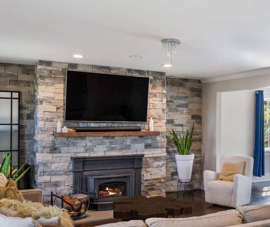 Living room with stone fireplace, TV, and armchair. A plant in a white pot and dark wood coffee table.