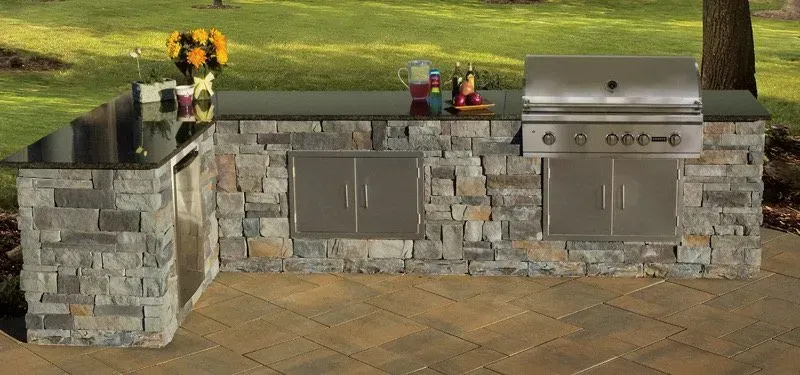 Outdoor kitchen with stone base, stainless steel appliances, and dark countertop.