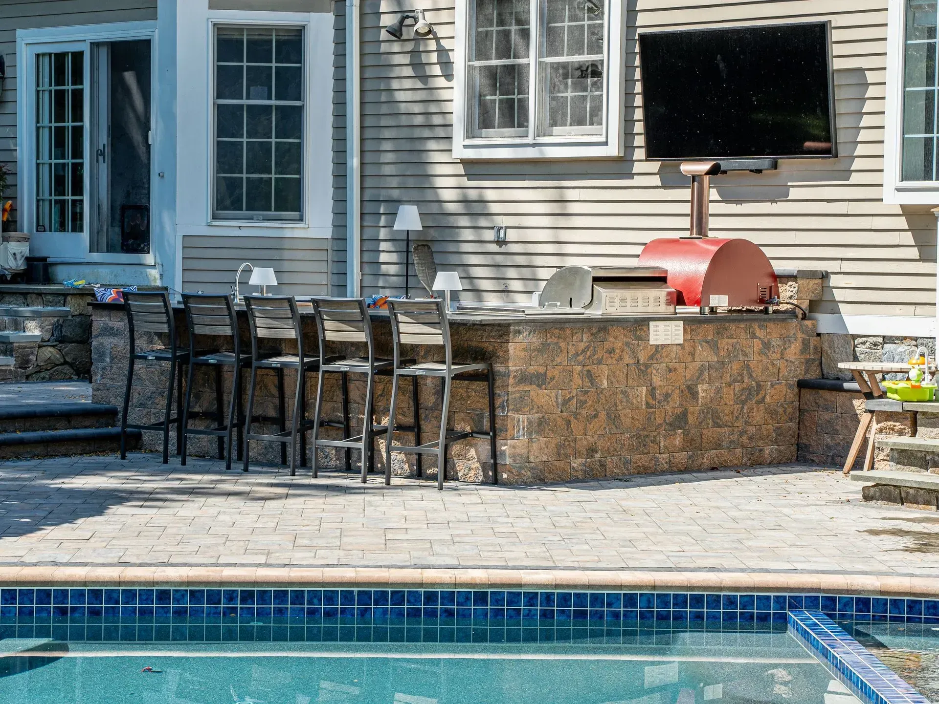 Outdoor kitchen with bar seating, a pool, and a mounted TV.