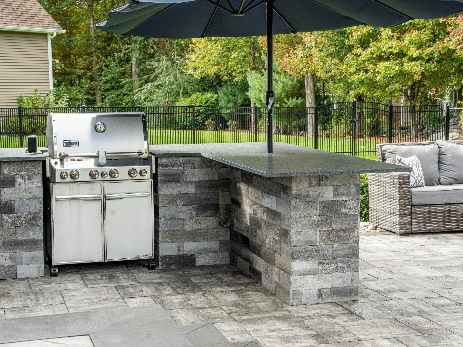 Outdoor kitchen with grill, countertop, umbrella, and seating on a patio.