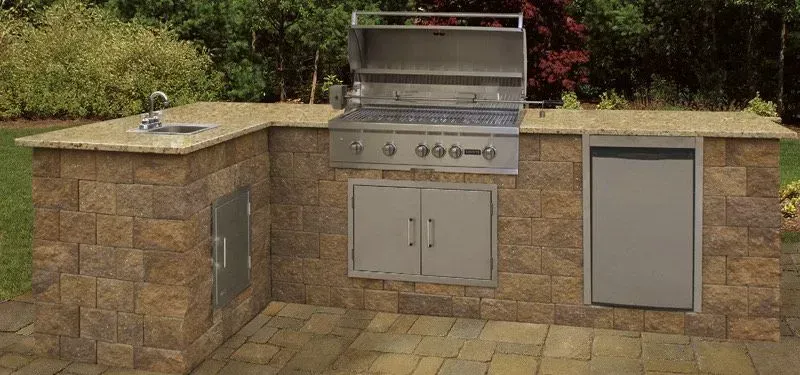 Outdoor kitchen with a grill, sink, and fridge, built of brown stone.