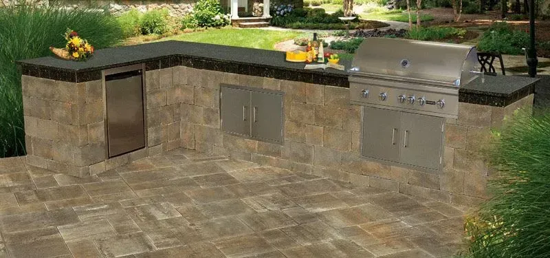 Outdoor kitchen with grill, refrigerator, and countertop made of stone blocks and dark gray countertop.