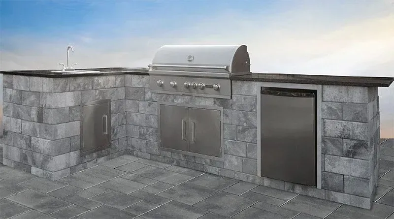 Outdoor kitchen with a grill, sink, and refrigerator, built into a gray stone structure.