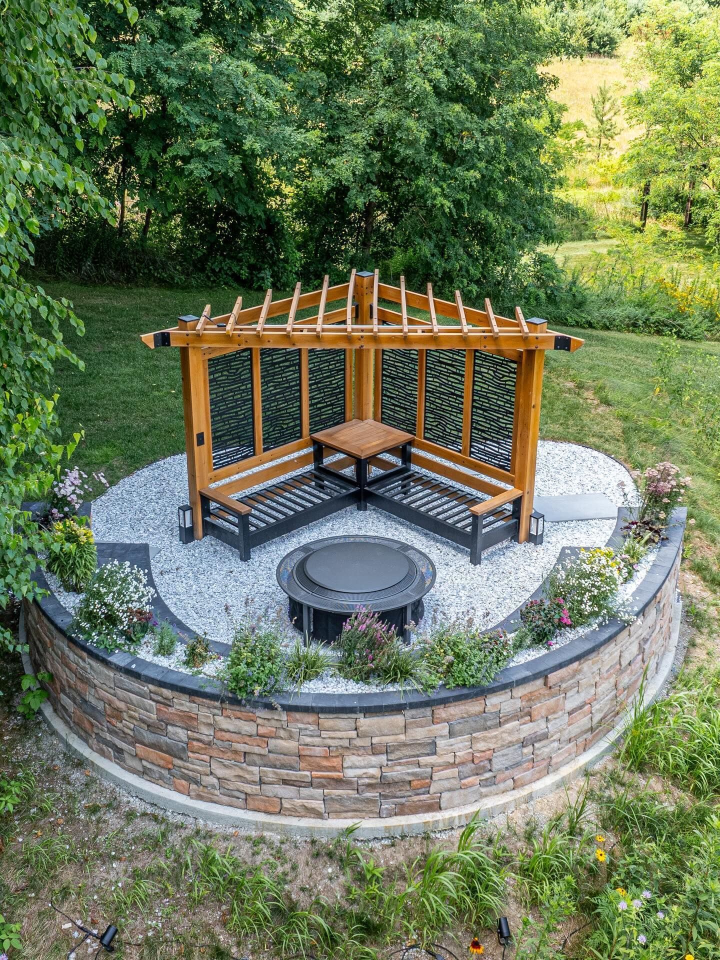 Gazebo with built-in benches, fire pit, stone wall, and landscaping in a garden setting.