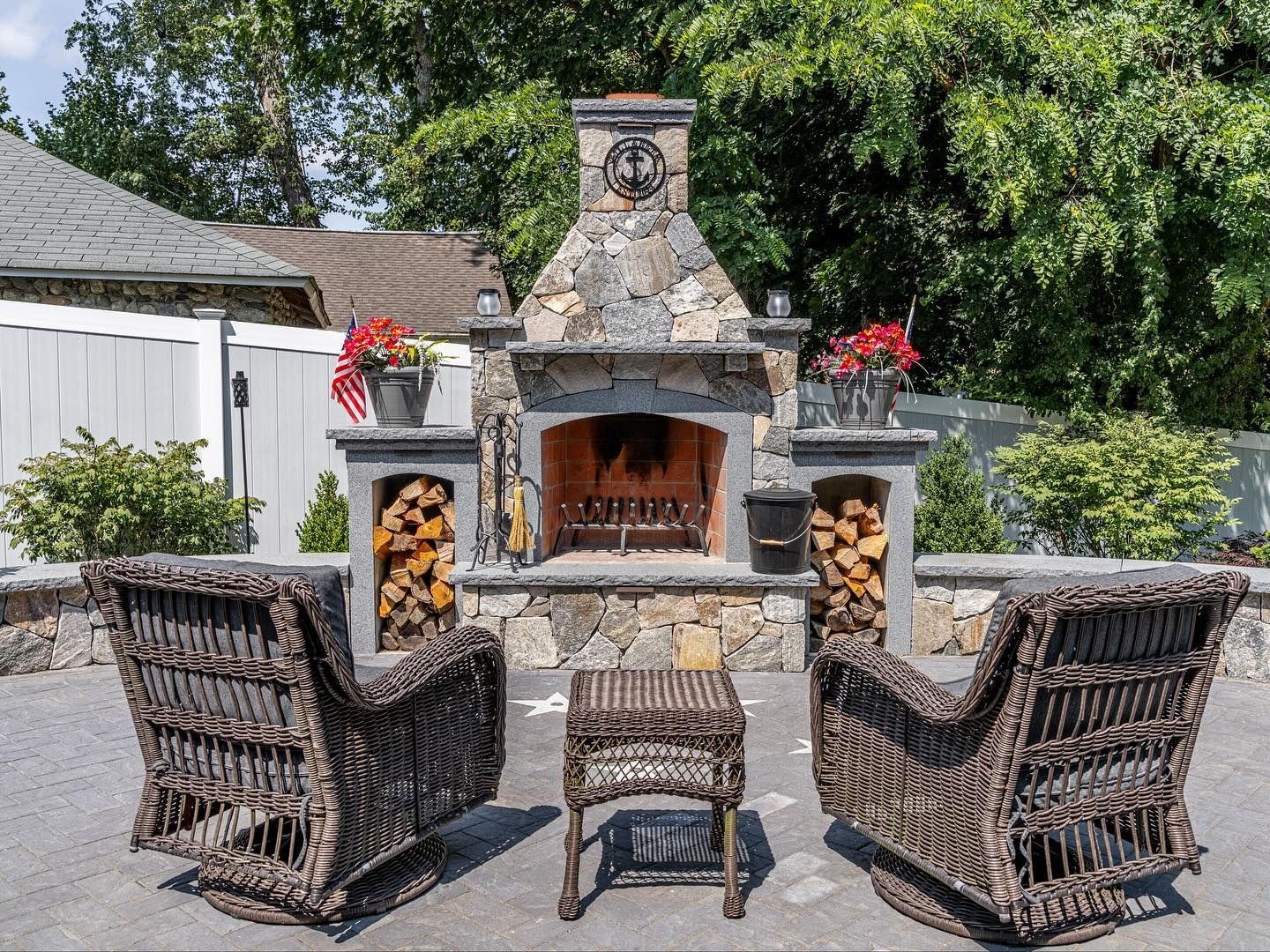 Outdoor stone fireplace with two wicker chairs and a small table on a patio.