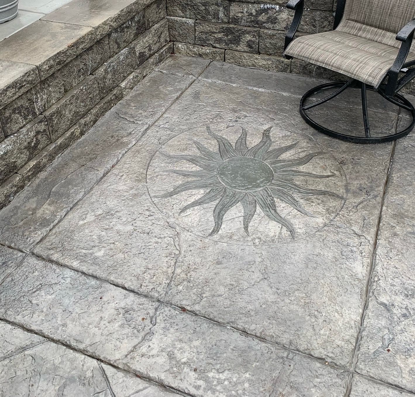 Concrete patio with sun design and chair.