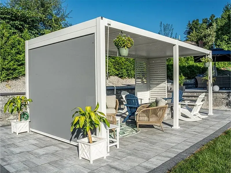 White pergola with gray sun shade, outdoor seating area, potted plants on a patio.