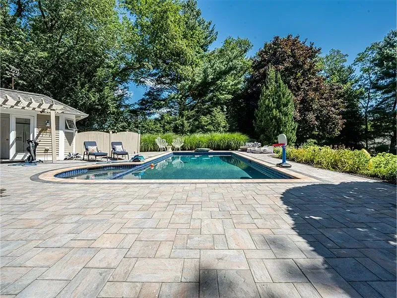 Swimming pool surrounded by stone patio, lounge chairs, and lush landscaping.