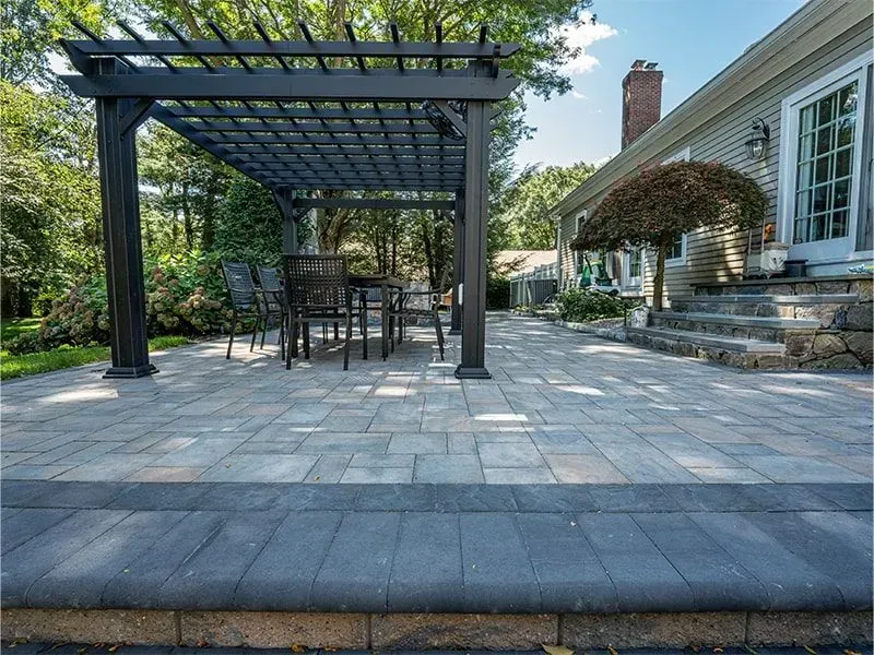 Patio with dark pergola, table, and chairs. Paver patio with steps leading to house.