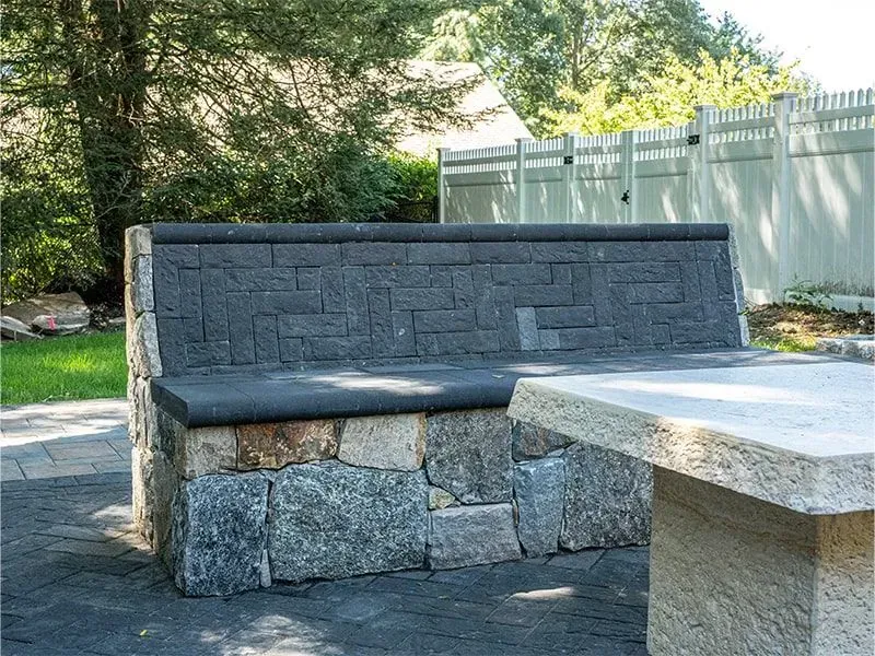 Stone bench with dark textured back and light stone base, next to a matching table, outdoors.