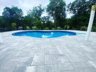 Swimming pool with blue water and gray stone patio. Trees in background.
