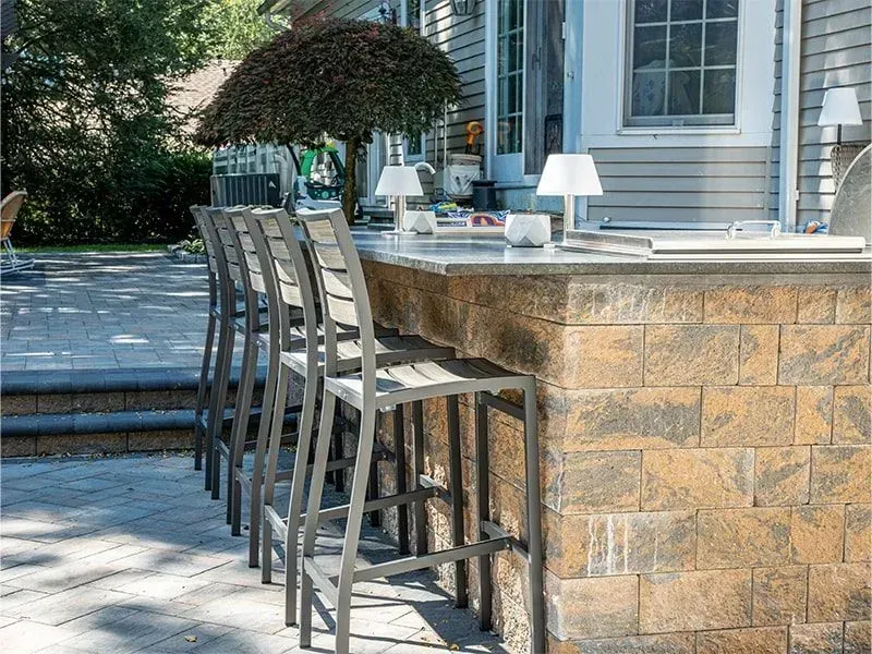 Outdoor bar with stone facade, gray stools, and countertop with white lamps.