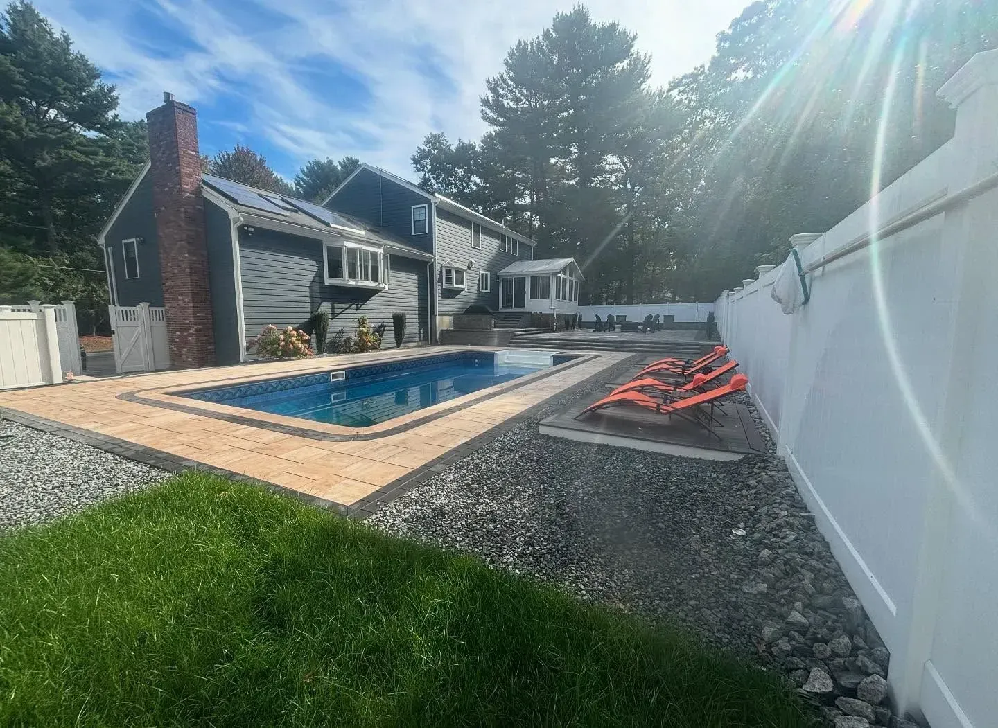 A backyard with a rectangular pool, gray house, white fence, and lounge chairs.