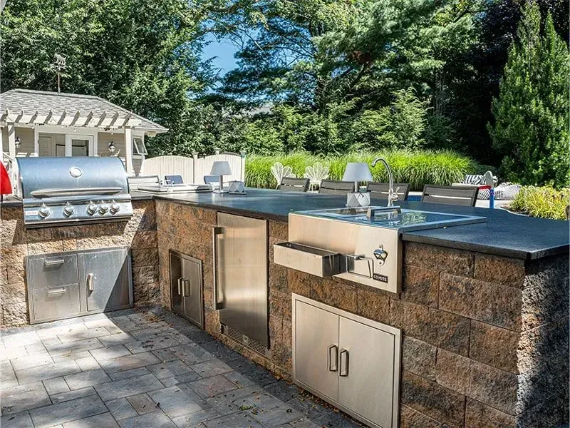 Outdoor kitchen with a grill, sink, refrigerator, and storage cabinets made of brick.