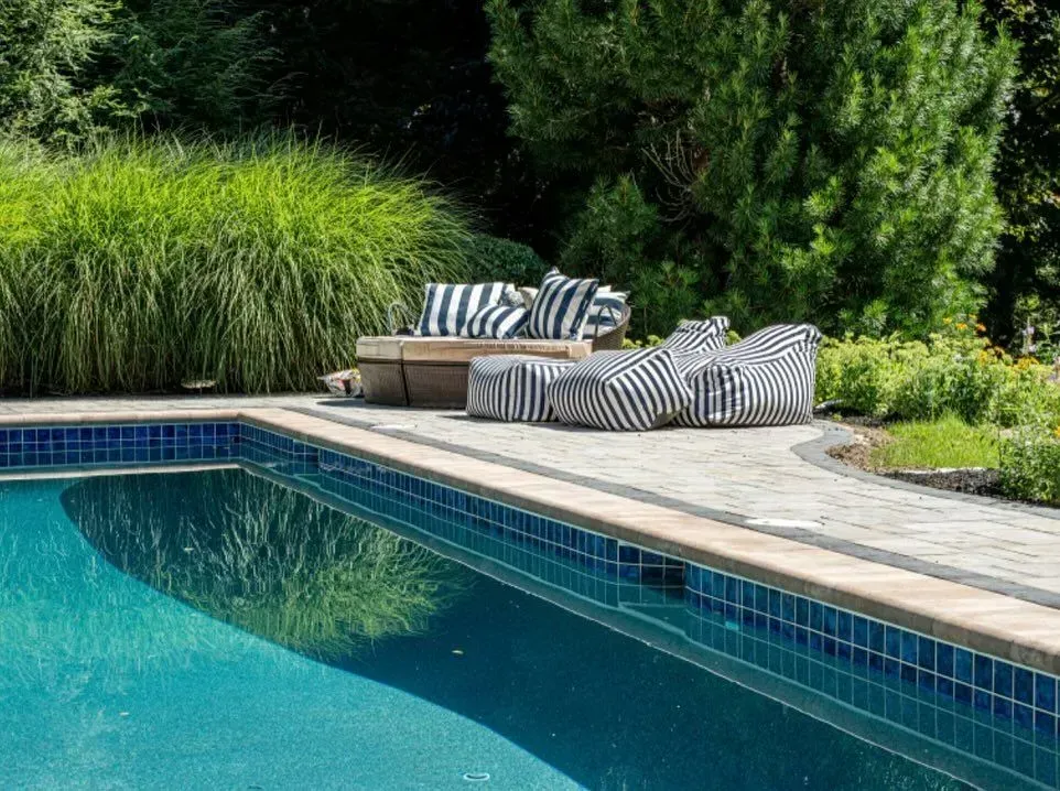 Poolside lounge area with striped cushions, overlooking a blue pool and greenery.