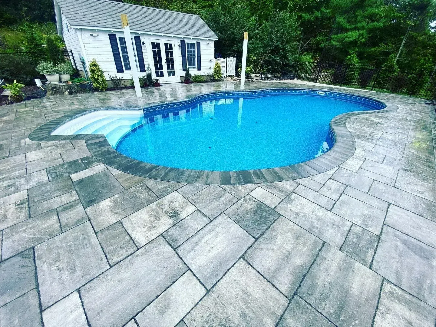 Pool with blue water and stone patio, small white house in background.