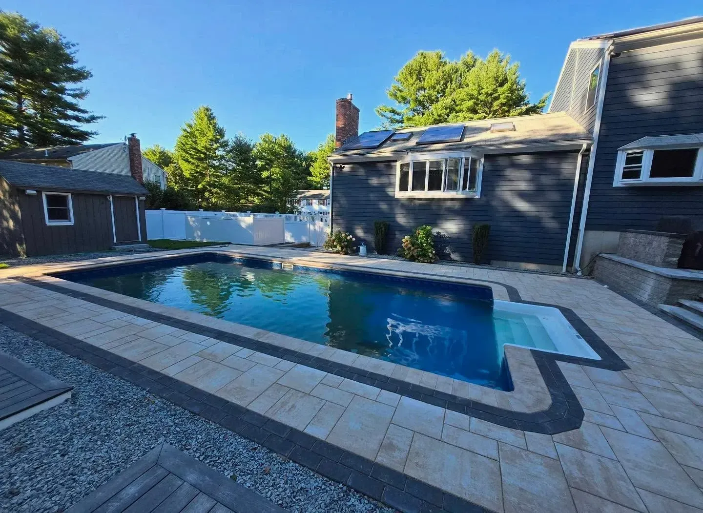 Backyard with a swimming pool, pavers, and a dark-colored house.
