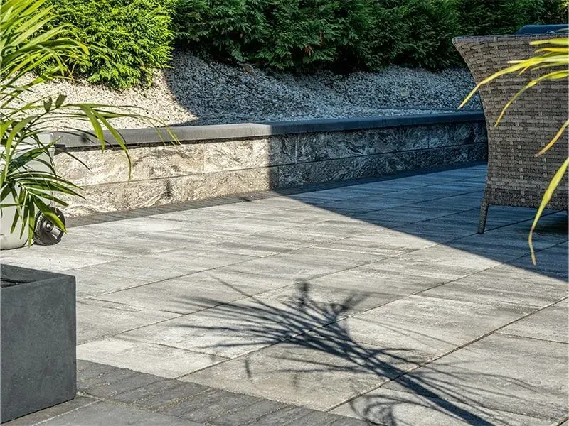 Patio with gray pavers, stone wall, greenery, and shadow.