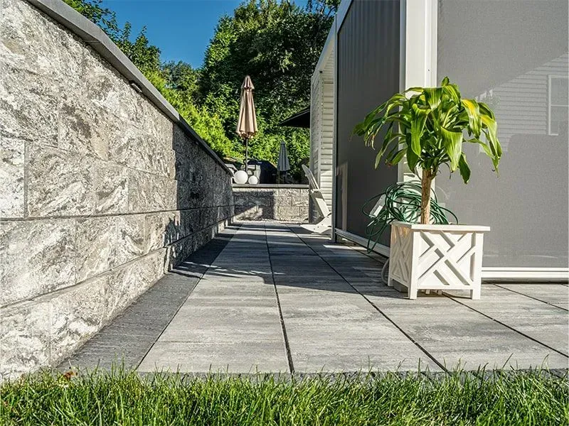 Stone patio with a wall, walkway, and a potted plant in a decorative planter.