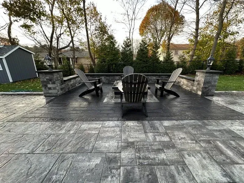 Patio with Adirondack chairs around a fire pit, surrounded by a stone wall and landscaping.