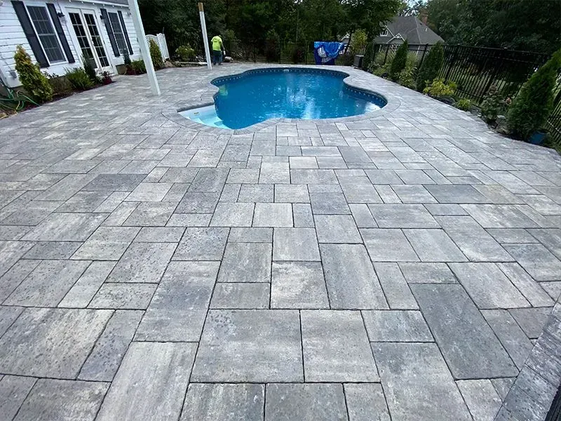 Gray stone patio surrounds a blue freeform pool. White house in the background.