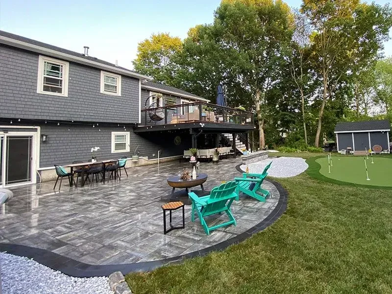 Backyard patio with deck, dining set, fire pit, lounge chairs, and putting green.