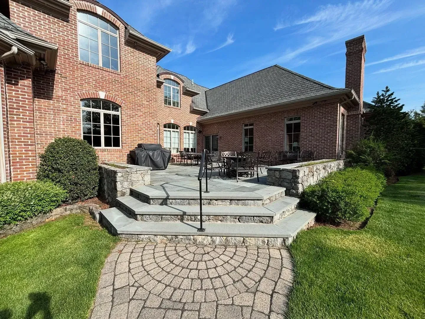 Brick home exterior with patio, steps, and landscaping on a sunny day.