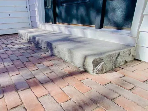 Brick patio with concrete steps leading to a dark doorway, sunlight casts shadows.
