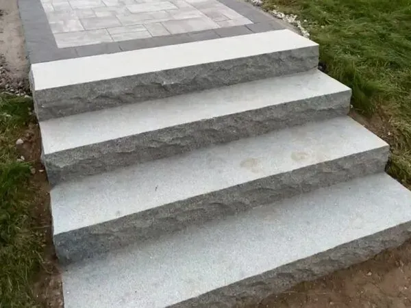 Granite steps leading up to a gray patio with surrounding grass.