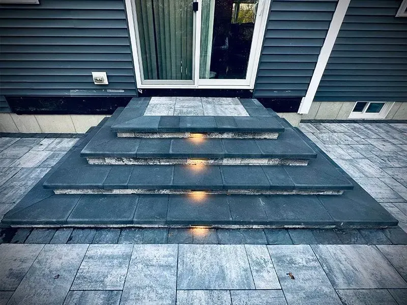Stone steps leading to a sliding glass door. Built-in lights illuminate each step. Exterior of a house.