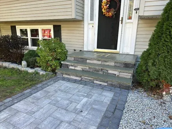 Stone steps leading to a house entrance with gray pavers and landscaping.
