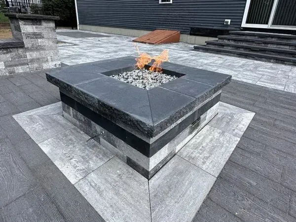 Stone fire pit with flames, on a paved patio.